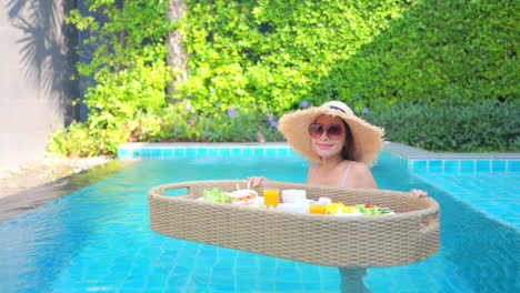 A-young-woman-in-a-luxury-swimming-pool-steadies-a-floating-breakfast-buffet