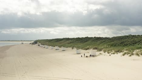 Aerial-shot-flying-over-a-beautiful-white-beach-and-green-dunes-on-a-cloudy-day