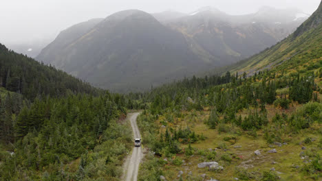 Car-driving-on-dirt-road-through-forest-valley-in-misty-British-Columbia,-aerial