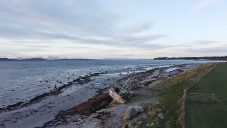 AERIAL---Shipwreck-on-a-beach-with-person-riding-horse,-Kintyre,-Scotland,-pan-left