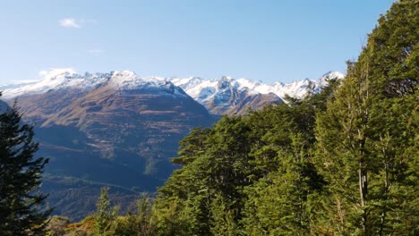 Panoramic-shot-of-massive-mountains-with-white-snowy-peak-on-top-during-sunny-day-at-hike-in-vegetated-national-park-of-New-Zealand