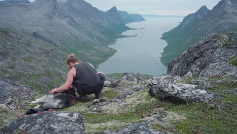 Ein-Kaukasischer-Männlicher-Wanderer,-Der-Seinen-Hund-Streichelt,-Während-Er-Sich-Auf-Einem-Felsigen-Berg-Im-Anderdalen-nationalpark-In-Senja,-Norwegen,-Ausruht