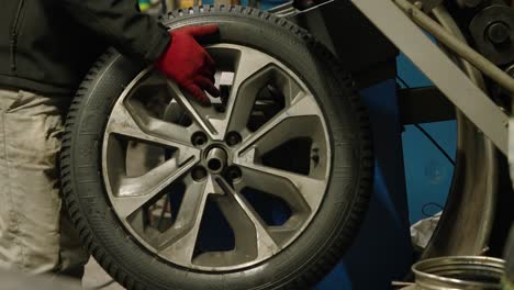 Close-up-of-wheel-mounted-on-tire-changer-with-operator-removing-it