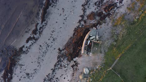AERIAL---Shipwreck,-boat-on-a-beach-at-sunset-in-Kintyre,-Scotland,-top-down-rising