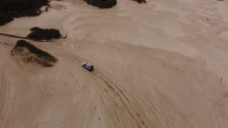 High-aerial-following-shot-of-the-four-Wheel-Car-leaving-beach-and-driving-on-rural-forest-road-beside-the-beach-water-waves-in-South-America-,-Argentina