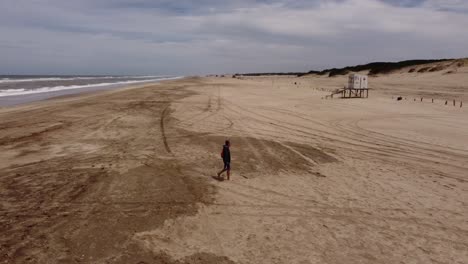 Zeitlupenaufnahme-Eines-Alten-Mannes,-Der-Auf-Dem-Sand-Vor-Den-Strandwasserwellen-Auf-Einem-Natürlichen-Hintergrund-In-Mar-De-Las-Pampas,-Argentinien,-Spaziert