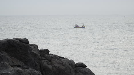 Fishing-vessel-leaving-rocky-shore-for-fishing-trip,-static-view