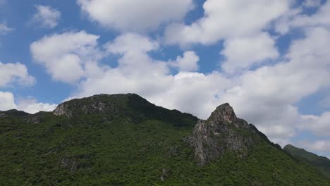 Lovely-cotton-like-clouds-and-the-mountain-with-rock-tower-jutting-out-while-this-aerial-footage-slides-to-the-left-in-Sam-Roi-Yot-National-Park,-Prachuap-Khiri-Khan,-Thailand