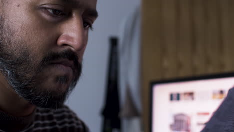 A-close-up-shot-of-an-Indian-man-sitting-in-front-of-his-computer,-reading-through-the-pages-and-reviewing-the-details-of-the-invoices-he-is-due-to-pay