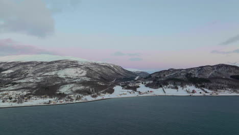 Drone-shot-flying-over-water-towards-a-snow-capped-mountain-in-Norway