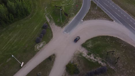 Aerial-top-view-of-a-black-car-driving-from-rural-road-to-main-route-in-natural-background-at-Mar-de-las-Pampas,-Argentina