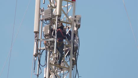 close-up-of-two-men-working-on-and-up-a-communication-tower-conducting-repairs-or-maintenance
