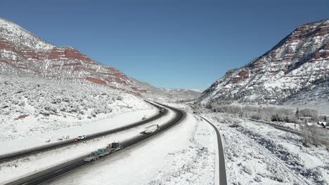 Following-semi-tractor-trailer-trucks-driving-along-I-70-in-the-mountains-with-fresh-snow-on-the-ground