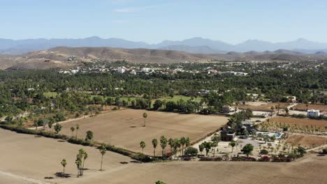 Side-slow-motion-shot-of-the-farm-land-in-Todos-Santos,-the-whole-town-full-of-small-green-bushy-trees,-houses-and-mountain-ranges-on-a-sunny-day-in-Mexico
