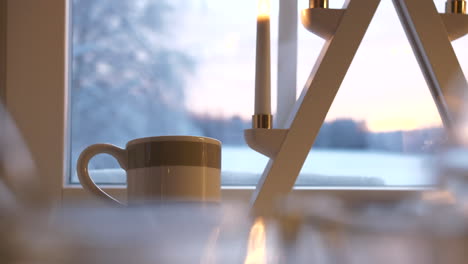 Hot-cup-of-tea-near-Christmas-decorations-and-window-with-winter-landscape-view