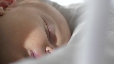 Close-up-of-face-of-baby-sleeping-in-swinging-crib-in-sunlight,-slomo