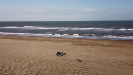 High-aerial-orbiting-view-of-the-family-and-parked-four-wheel-drive-on-the-beach-side-at-a-beautiful-sunrise-morning-in-holidays-in-Mar-de-las-Pampas,-South-America