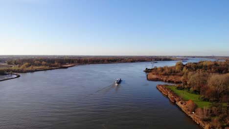 Aerial-View-Over-Autumnal-Landscape-Next-To-Oude-Maas-With-Ship-Going-Past-In-Background