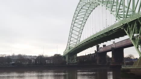 Runcorn-Silver-Jubilee-suspension-bridge-reflections-rippling-in-River-Mersey-below-pan-left-tilt-down