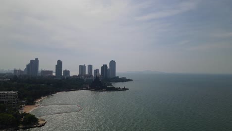 Ascending-aerial-footage-revealing-a-beachfront-and-hotels-plus-the-Sanctuary-of-Truth-silhouetting-in-Pattaya,-Chonburi,-Thailand