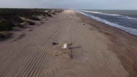 Aerial-following-shot-of-the-four-Wheel-Car-leaving-beach-and-driving-on-rural-forest-road-beside-the-beach-water-waves-in-South-America-,-Argentina