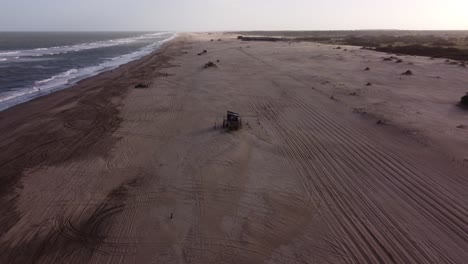 Aerial-following-shot-of-the-four-wheel-car-on-the-sandy-track-beach,-driving-on-rural-forest-road-beside-the-beach-water-waves-in-South-America-,-Argentina