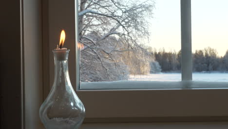 Kerzenlicht-In-Der-Flasche-Neben-Dem-Fenster-Zu-Hause-Mit-Verschneiter-Landschaft-Draußen