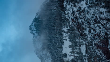 Vertical-Time-Lapse-of-Freezing-Cold-Winter-Landscape-in-Mountains,-Dark-Clouds-Moving-Above-Snow-Capped-Hills-and-Forest