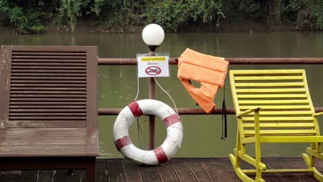 A-warning-sign-advising-people-of-no-swimming-in-the-fast-flowing-waters-of-the-Khwae-river,-safety-equipment-is-provided-in-the-case-of-an-emergency-in-Kanchanaburi,-Thailand
