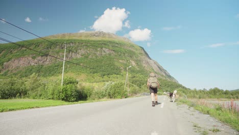 Hombre-Viajero-Tirando-De-Su-Perro-Con-Correa-Cruzando-La-Carretera-Que-Conduce-A-Una-Montaña-En-Lyngsdalen,-Noruega