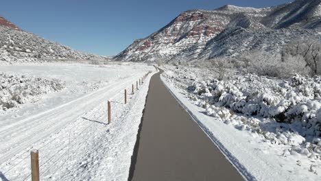 Aerial-footage-along-a-bike-path-as-it-travels-towards-red-mountains-and-cliffs-along-Interstate-70