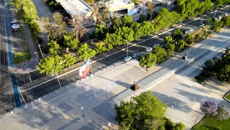 Aerial-orbit-of-the-Chilean-flag-waving-in-vitacura's-bicentennial-park-with-people-walking-on-their-walkways---drone-shot