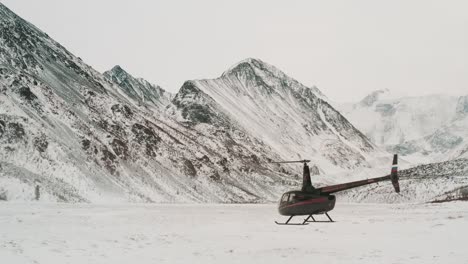 Helicopter-taking-off-from-desolate-snow-covered-alpine-mountains
