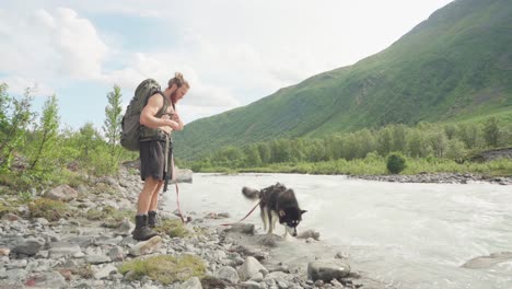 Mochilero-Macho-Con-Un-Perro-Deja-De-Caminar-Refresca-Su-Cuerpo-Con-Agua-De-Un-Río-Rocoso-En-El-Valle-De-Lyngsdalen,-Noruega