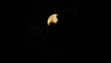 Black-clouds-slowly-blow-away-revealing-light-yellow-full-moon-in-night-sky