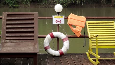 A-tilt-reveal-shot-of-two-loungers-on-the-deck-of-a-houseboat-on-the-Khwae-river,-people-are-advised-not-to-swim-and-safety-equipment-is-provided-in-the-case-of-an-emergency-in-Kanchanaburi,-Thailand