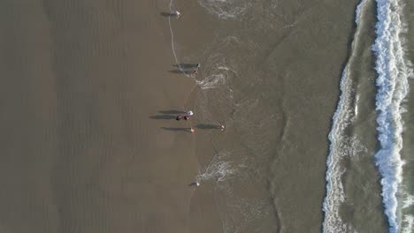 Aerial-view-of-people-walking-at-the-beach-with-waves-rolling-at-the-shore