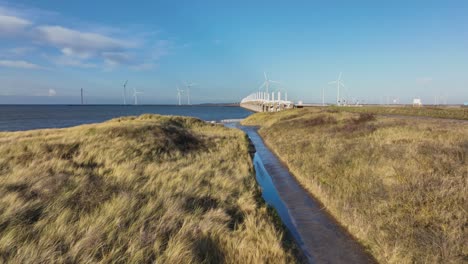 Aerial-shot-flying-over-a-path-through-the-dunes-towards-the-Eastern-Scheldt-storm-surge-barrier-in-Zeeland,-the-Netherlands,-on-a-beautiful-sunny-day