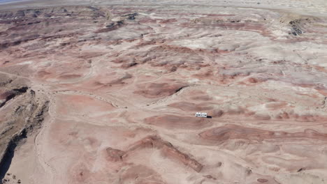 An-aerial-shot-of-an-RV-driving-through-the-Utah-desert-with-crazy-rock-formations-on-an-American-roadtrip