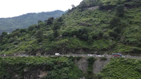 A-drone-shot-of-commercial-vehicles-traveling-on-a-suspended-bridge-on-a-river-valley-in-the-remote-highway-of-Himachal-Pradesh,-at-the-foothills-of-the-Indian-Himalayas