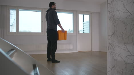 Young-man-picks-up-last-box-from-empty-room-when-moving-out,-static
