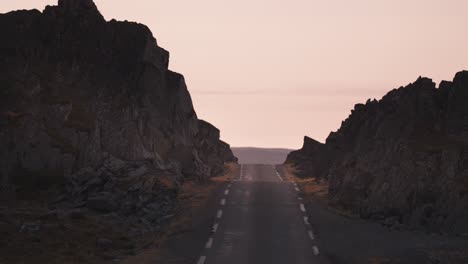 Driving-on-the-narrow-asphalt-road-along-the-rocky-shores-of-the-fjord-in-the-warm-light-of-the-sunset