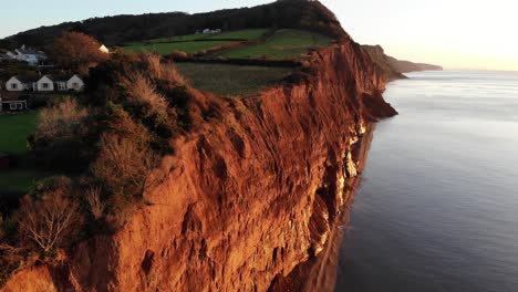 Aerial-shot-of-the-red-Jurassic-Cliffs-at-Sidmouth-Devon-England-at-sunrise-bathed-in-golden-sunlight