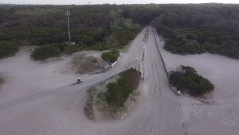 Aerial-view-of-a-person-driving-a-motorbike-on-the-beach-sand-in-a-forest-background-in-Mar-de-las-Pampas,-South-America