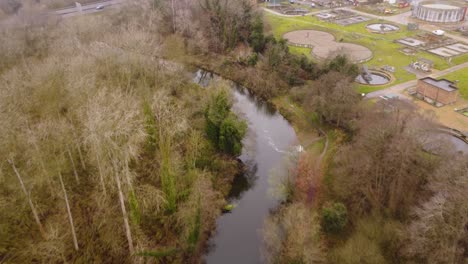 River-through-forest-beside-wastewater-treatment-plant-in-Thetford,-Norfolk---aerial-drone-flight-shot-:-rural-area-with-road