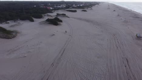 Aerial-following-shot-of-motorbike-driving-on-sandy-beach-during-cloudy-day