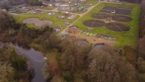 Aerial:-Sewage-wastewater-treatment-plant-beside-a-river-in-Thetford,-Norfolk---drone-backward-flight-shot-:-forest-destruction-for-industrial-plant