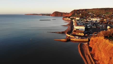 Aerial-Hugging-Along-Coastline-With-Sidmouth-Town-Bathed-In-Golden-Sunrise-Light