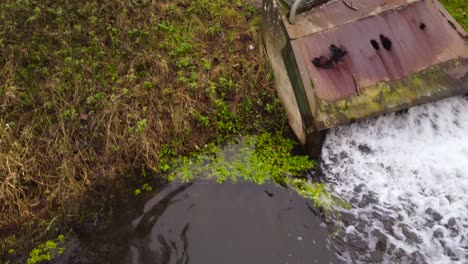 Contaminación-Del-Agua,-Aguas-Residuales-De-Fábrica-Que-Fluyen-En-El-Río-Desde-Una-Tubería-Oxidada---Dolly-Tiro-Inclinado-Hacia-Atrás