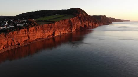 Luftaufnahme-Von-Roten-Sandsteinfelsen-Der-Jurassic-Coast-Bei-Sidmouth-Devon-England-Mit-Einem-Wunderschönen-Ruhigen-Meer-Bei-Sonnenaufgang